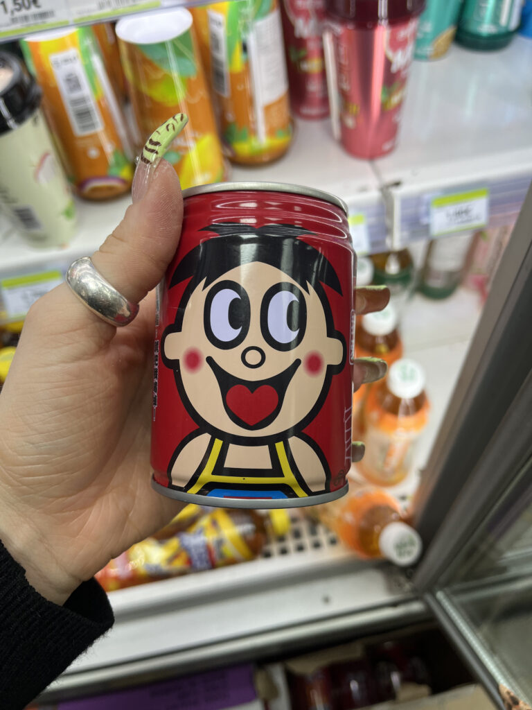 Lata de bebida con ilustración de niño sonriente en estilo retro japonés, fondo rojo y detalles llamativos.