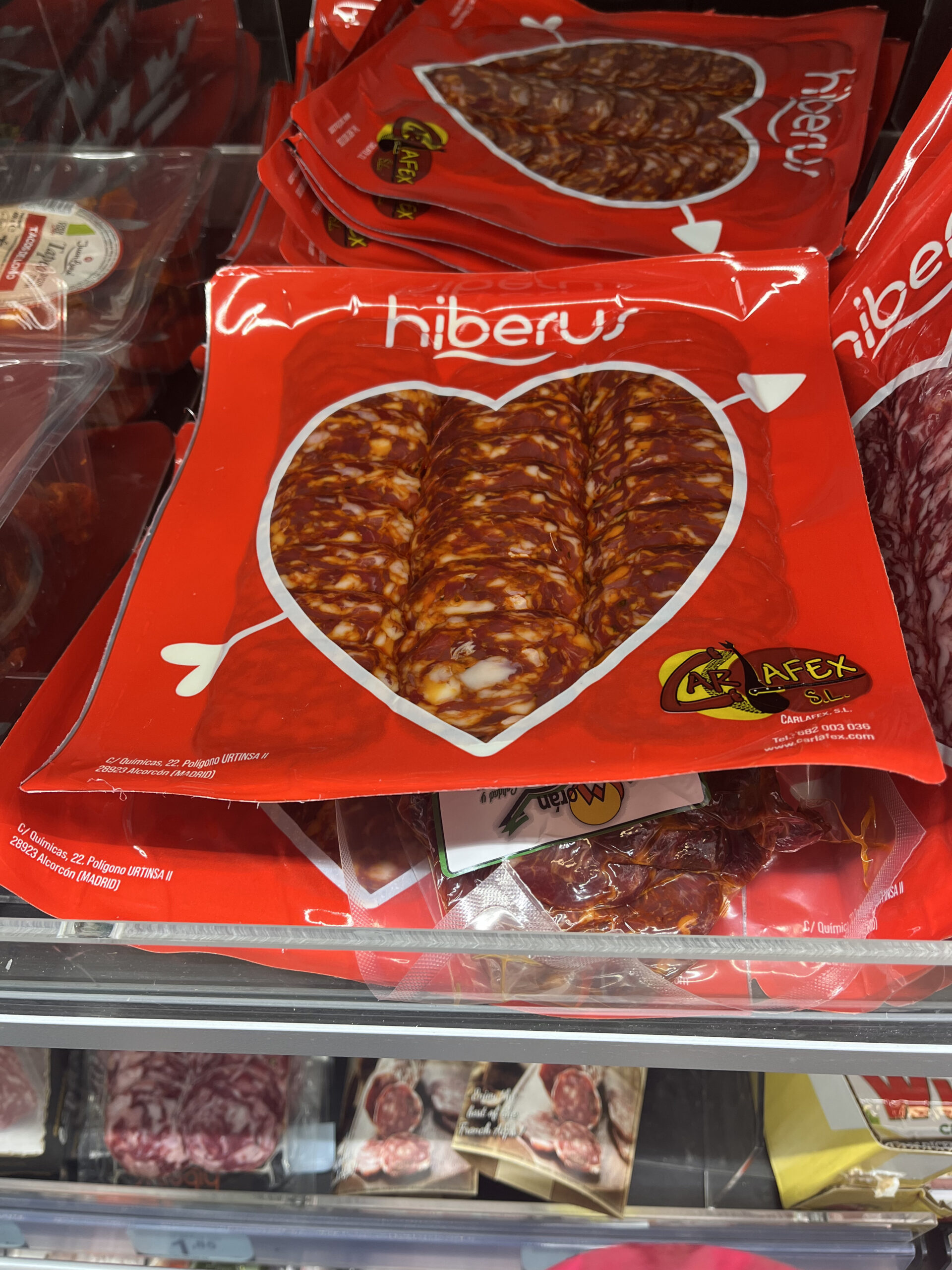 Envase de embutido Hiberus en forma de corazón con tipografía blanca sobre rojo y flecha gráfica decorativa.